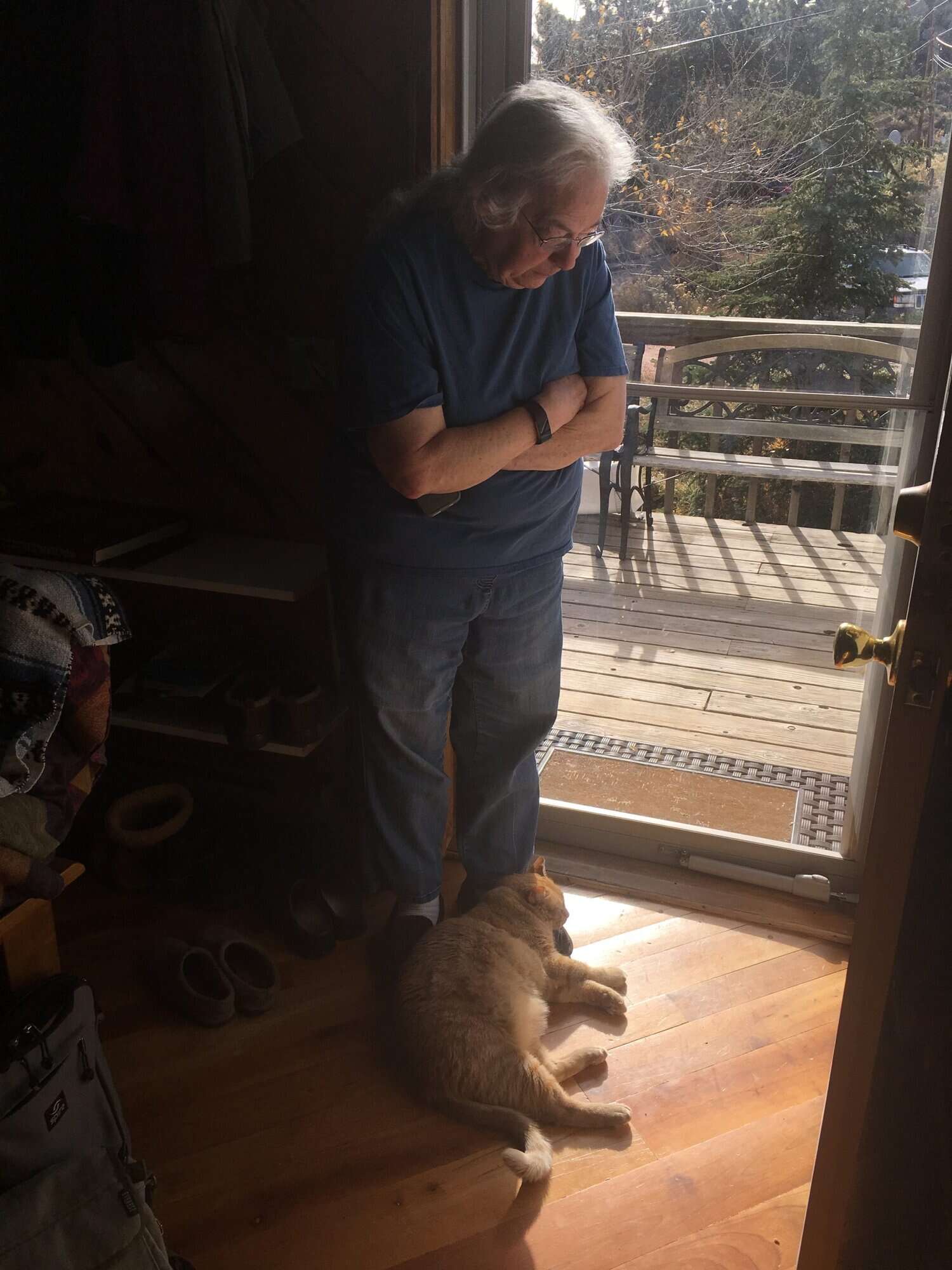 Susan standing in a doorway looking down at an orange cat lying on her feet