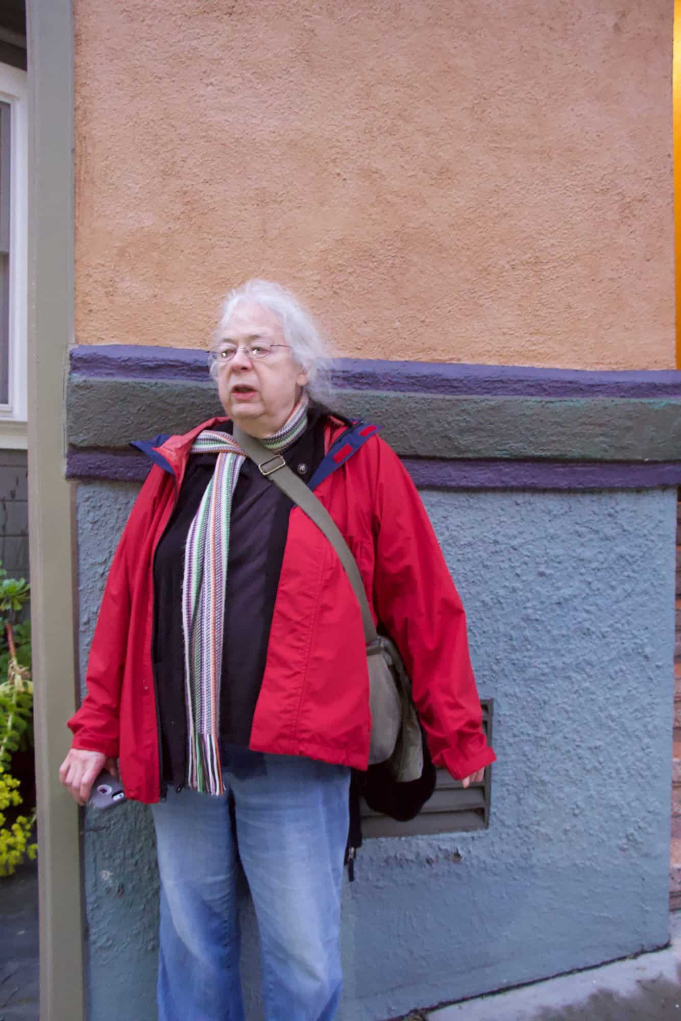 Susan standing in front of a blue and pink-orange stucco wall in San Francisco